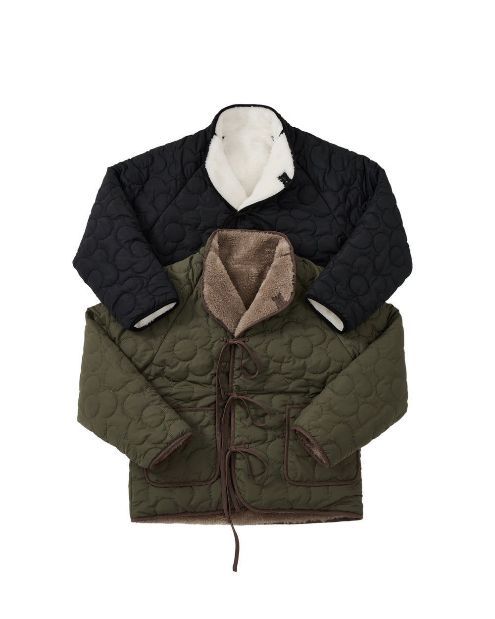 Two BLACK IVORY REVERSIBLE FLOWER QUILTED JEOGORI FLEECE jackets from Sundae School, one in black with white lining on top and the other in olive green with brown lining beneath, are neatly arranged, overlapping each other. Both showcase tie closures and visible stitching, drawing inspiration from classic hanbok-inspired coat silhouettes to seamlessly blend timeless style with modern comfort.