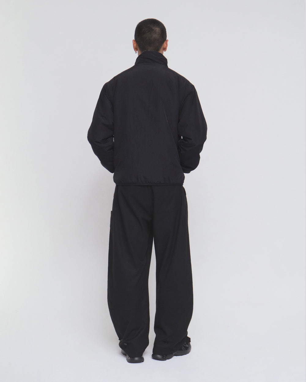 A person with short hair stands facing away, wearing the Sundae School BLACK REVERSIBLE IREZUMI FLEECE—featuring a bold tiger and dragon graphic—paired with loose black pants and black shoes against a plain white background.