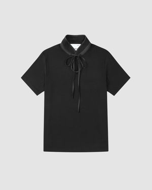 The BLACK RIBBON TIE POLO by Sundae School is a short-sleeved black shirt with a Manchurian teardrop collar and a long ribbon tie at the neck, shown against a plain light gray background.