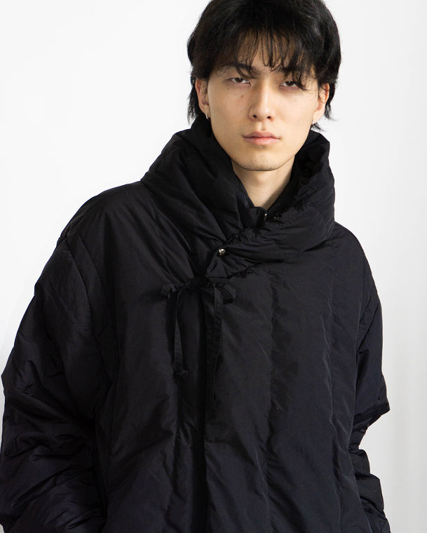 The BLACK HEAVYWEIGHT MOCHI PUFFER by Sundae School is a black puffer jacket with a large hood, long sleeves, and snap-closure cuffs, shown flat on a light gray background.