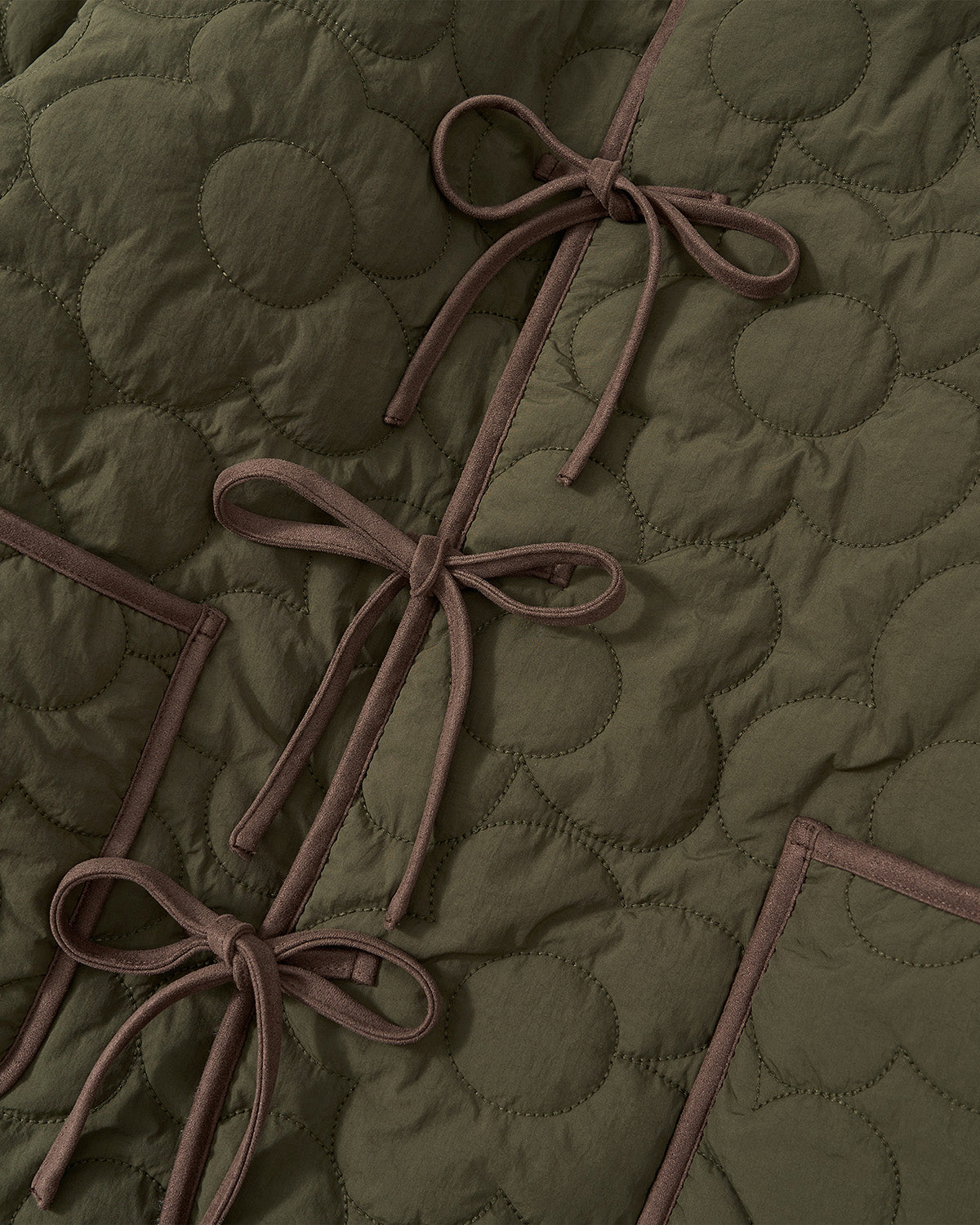 Close-up of an olive green quilted fabric with circular stitching, brown edging, and three bows—distinctive details from the Sundae School [PRE-ORDER] REVERSIBLE FLOWER QUILTED JEOGORI FLEECE. The texture and refined stitching are clearly visible.