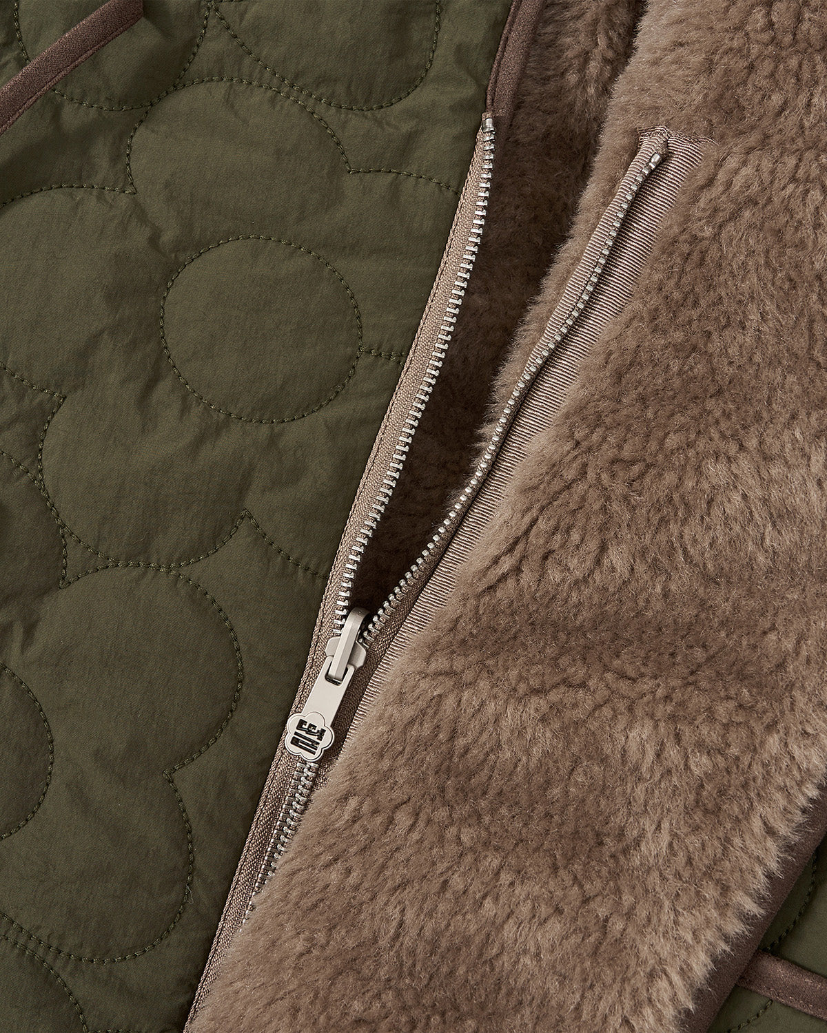 Close-up of Sundae School’s [PRE-ORDER] REVERSIBLE FLOWER QUILTED JEOGORI FLEECE, showcasing olive green quilted floral fabric on one side and soft brown fleece on the other, with an asymmetric closure and a partially open silver zipper.