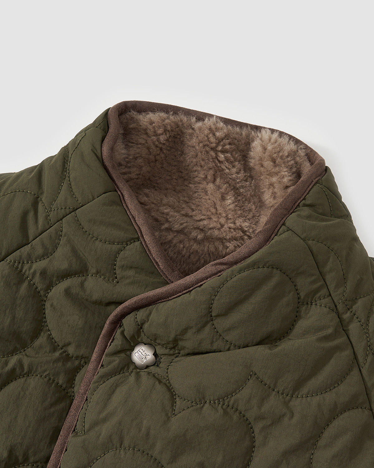 Close-up of Sundae School's REVERSIBLE FLOWER QUILTED JEOGORI FLEECE: a green, hanbok-inspired jacket with circular quilting, brown trim, visible soft sherpa fleece lining at the collar, and a front silver snap button.