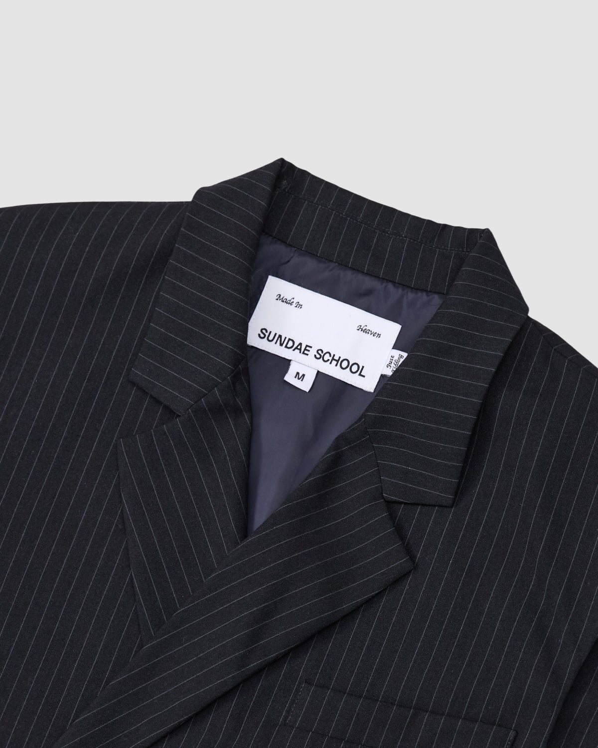 Close-up of the collar and label on a black pinstripe SABRINA VEST by Sundae School, featuring white vertical lines. The label inside shows the brand name, size M, and Made in Vietnam.