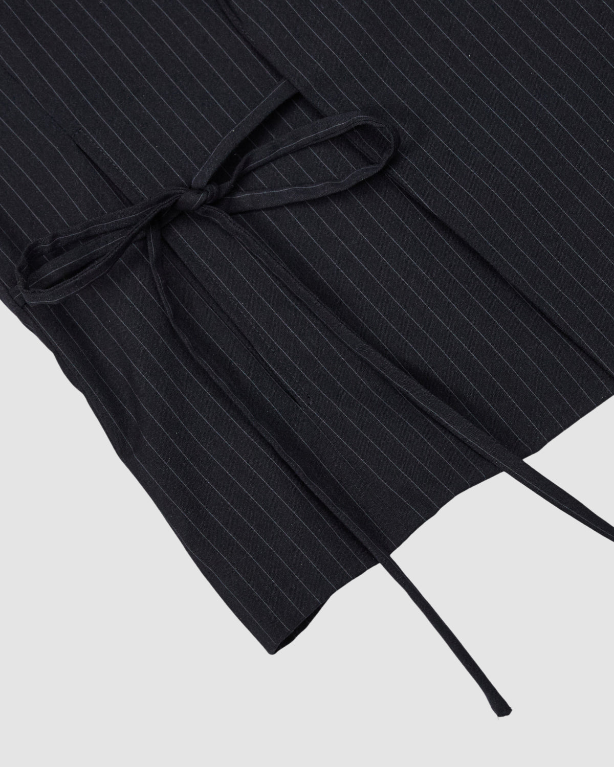 Close-up of the SABRINA VEST by Sundae School in black pinstripe summer wool with thin white lines, featuring a neatly tied Korean goreum tie bow made from matching fabric on a light gray background.