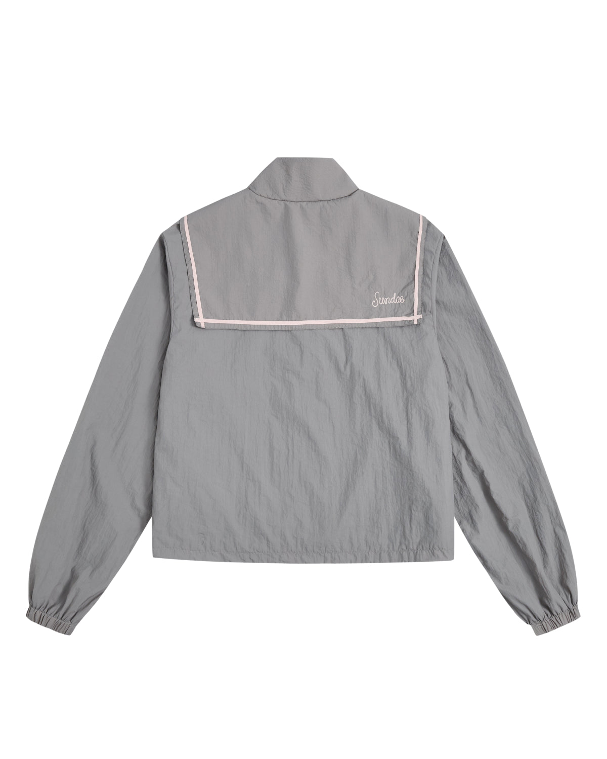 The GREY SAILOR WINDBREAKER by Sundae School is a light gray long-sleeve jacket designed in a classic sailor style, complete with a distinctive back flap, crisp white trim, and a small embroidered logo on the upper right. Crafted from lightweight, slightly textured fabric, this cropped windbreaker is perfect for breezy days.
