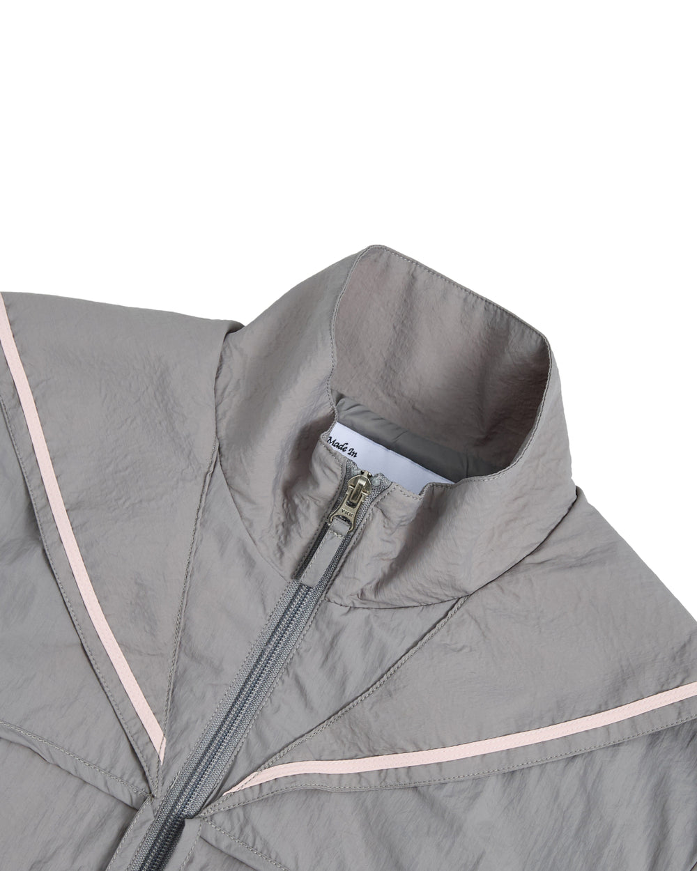 The GREY SAILOR WINDBREAKER by Sundae School is a light gray cropped jacket featuring a high collar, partial zipper, and light pink V-shaped accents on the chest. Made from lightweight, slightly crinkled fabric, this windbreaker is perfect for UV protection. Only the upper section of the jacket is shown.