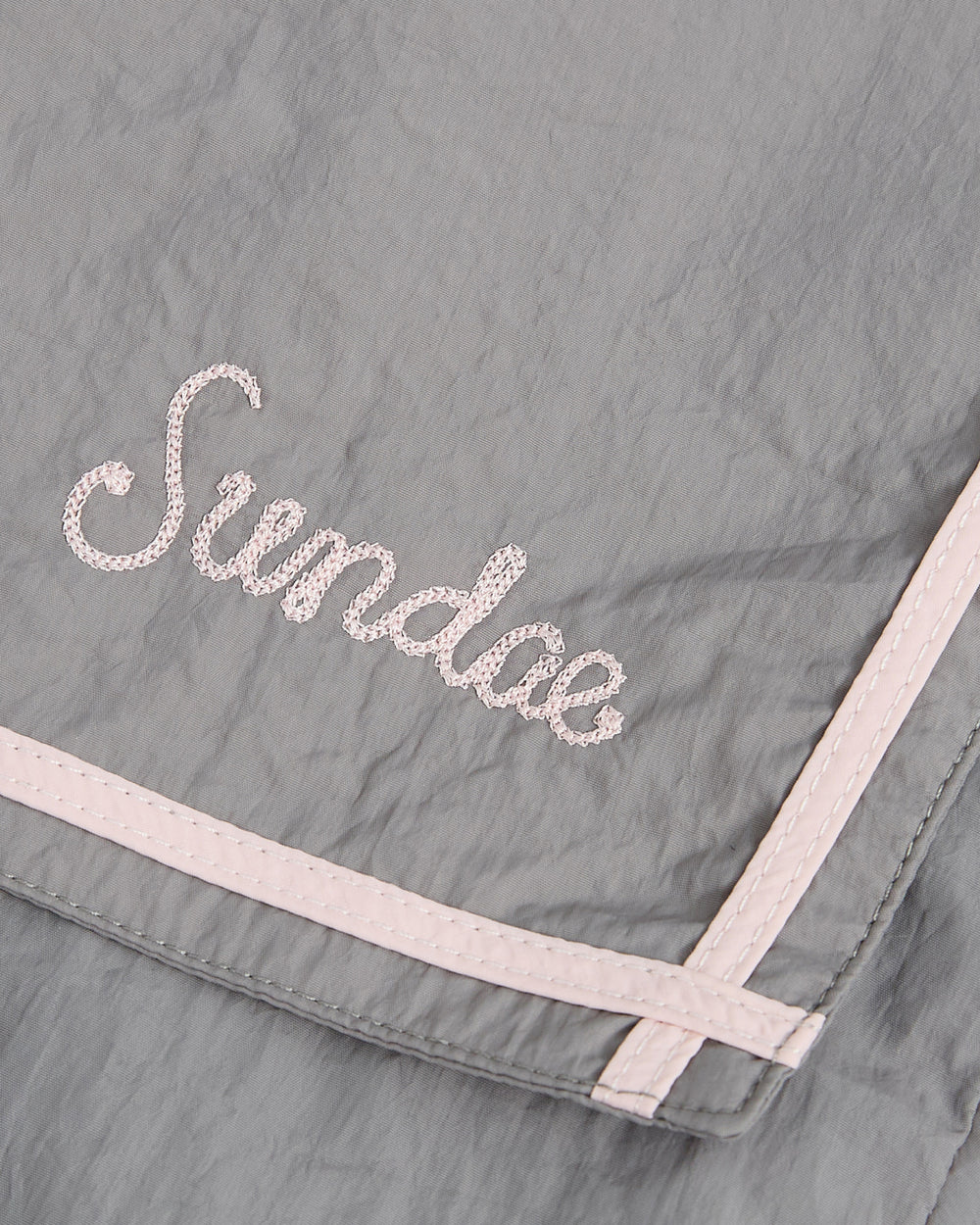 A gray fabric cropped windbreaker from Sundae School featuring light pink trim and “Sundae” embroidered in pink cursive lettering, called the GREY SAILOR WINDBREAKER.