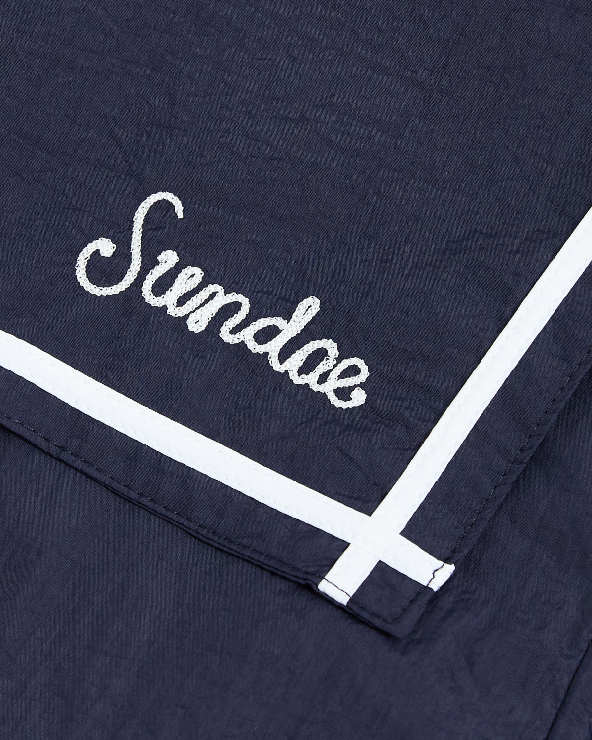 A close-up of dark blue fabric with white trim from the NAVY SAILOR WINDBREAKER by Sundae School, featuring 