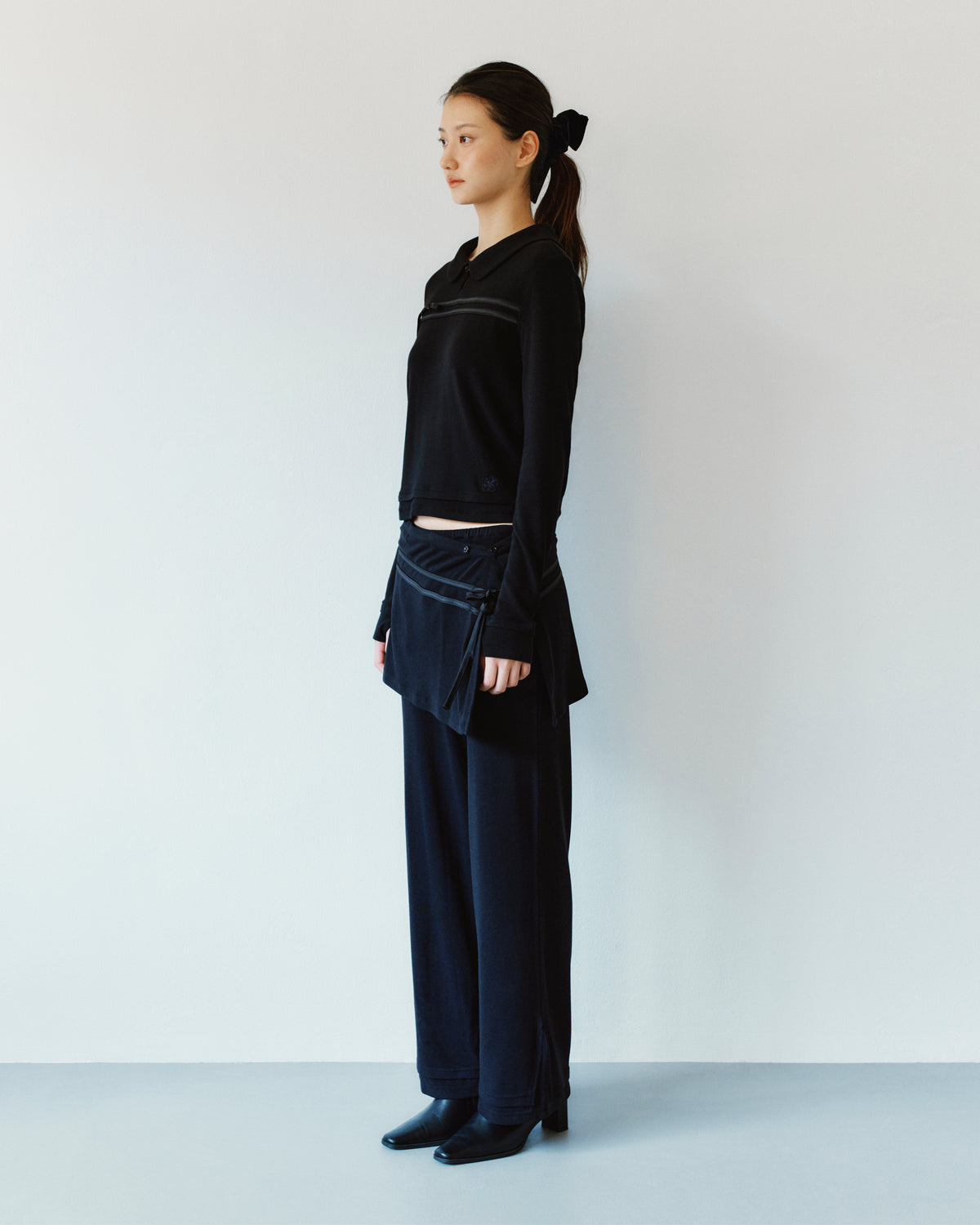 A person wearing a black long-sleeved polo shirt, BLACK SEONGSU APRON PANTS, and black ankle boots.