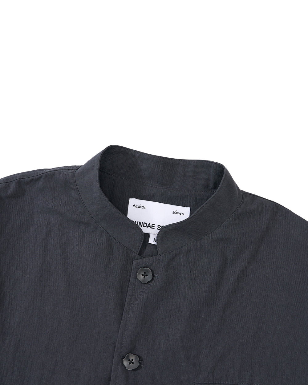 A close-up of the Sundae School CHARCOAL STAND COLLAR UNIFORM JACKET, made from a soft cotton-nylon blend with two buttons, set against a light grey background. A white label is visible inside the collar.