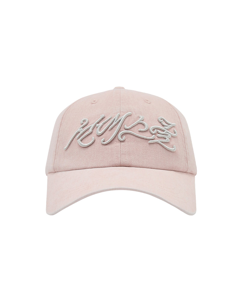 The BABY PINK DAENGGI CAP by Sundae School is a light pink, adjustable cotton cap featuring white embroidered stylized cursive text on the front, shown against a plain white background. This cap combines comfort and style.