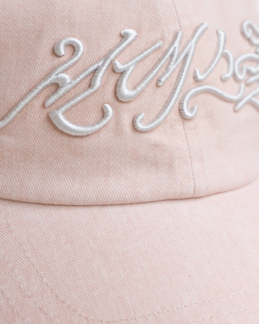 A close-up of the BABY PINK DAENGGI CAP by Sundae School, featuring raised white embroidered cursive on the front. This adjustable cotton cap showcases a soft texture and visible stitching.