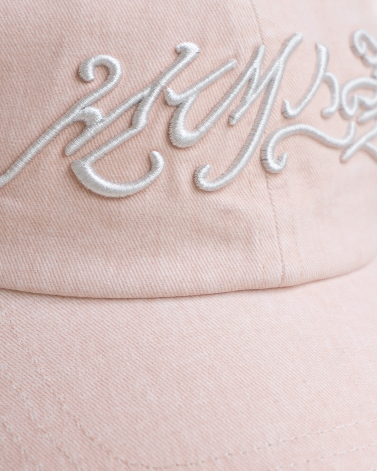 A close-up of the BABY PINK DAENGGI CAP by Sundae School, featuring raised white embroidered cursive on the front. This adjustable cotton cap showcases a soft texture and visible stitching.