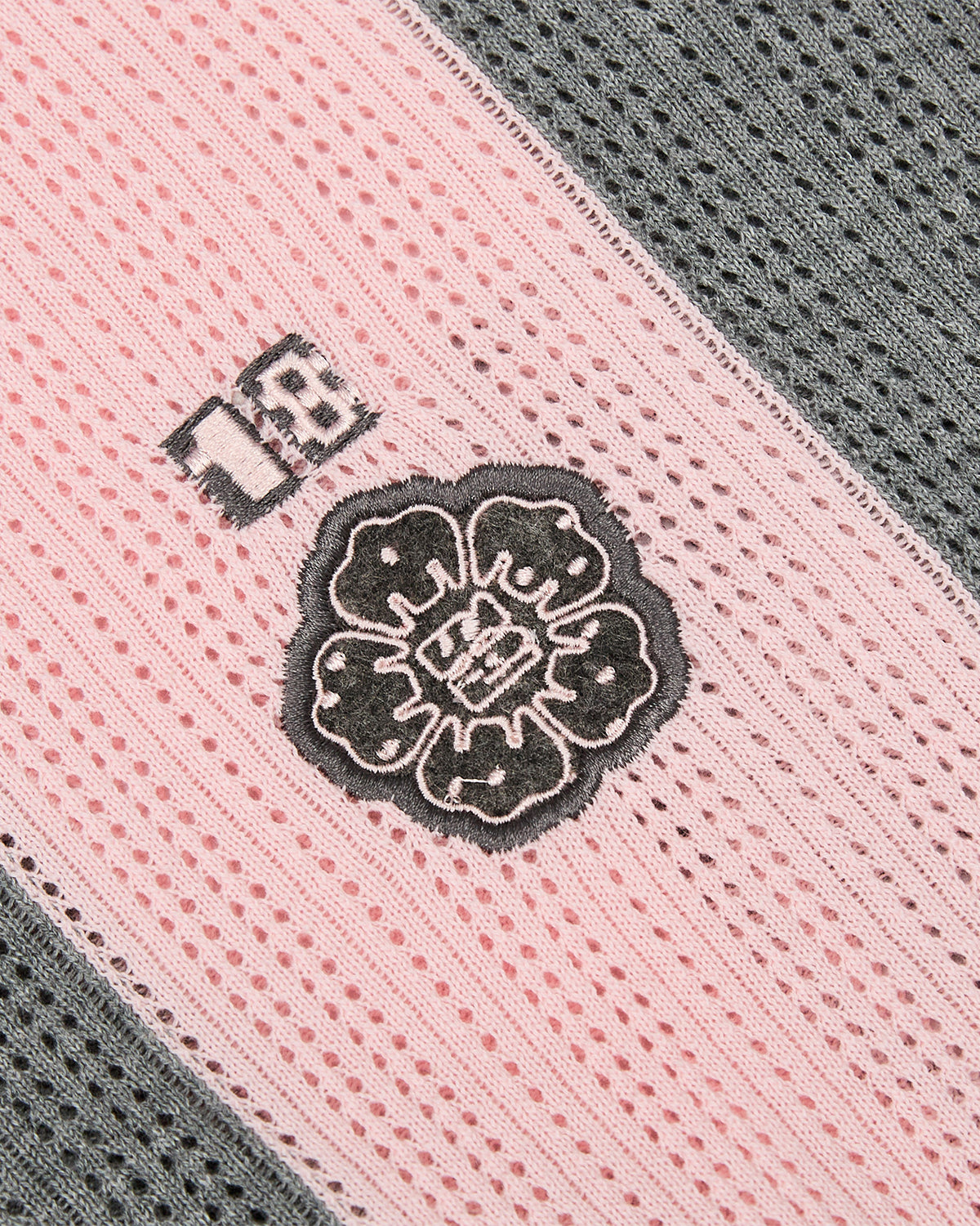 A close-up of the Sundae School PINK SUNDAE SOCCER JERSEY, a 100% cotton lightweight top with pink and gray lace-like stripes, a black embroidered flower, and a custom patch featuring the number 18.