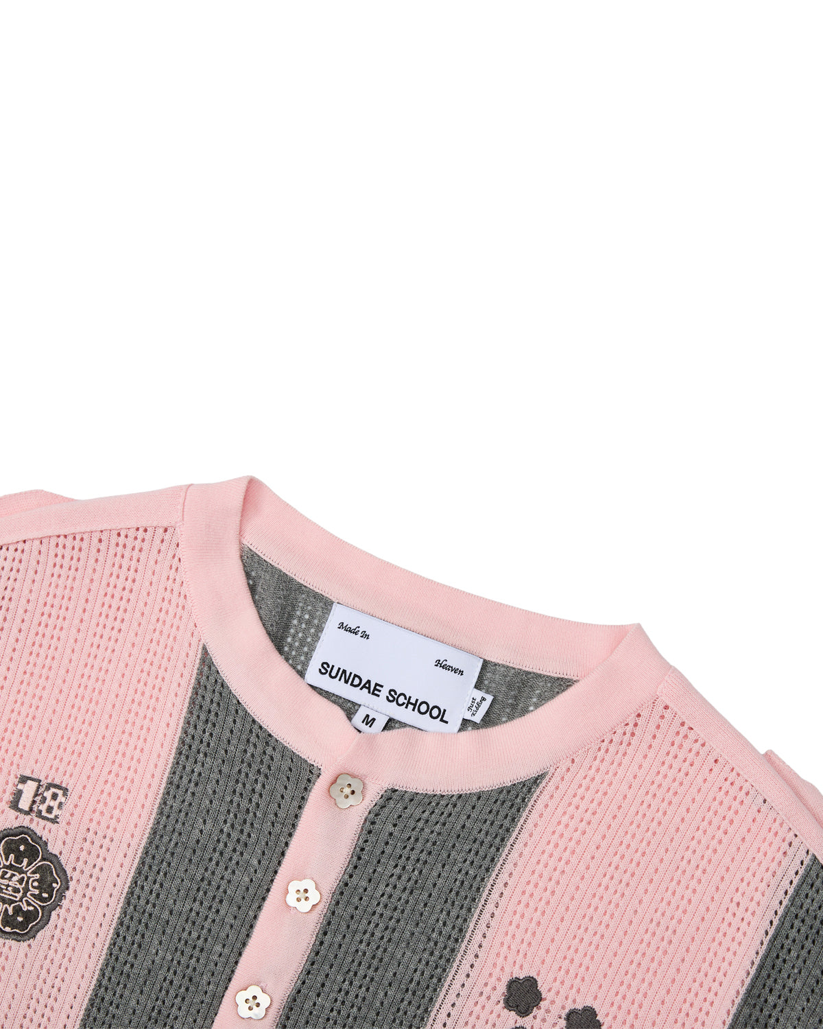 A close-up of the PINK SUNDAE SOCCER JERSEY by Sundae School showcases its ribbed design with pink and gray stripes, button accents, custom embroidered chest patches, and a prominent SUNDAE SCHOOL label at the collar. Crafted from 100% cotton, this lightweight top features perforated knit construction for enhanced breathability and comfort.