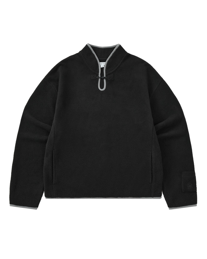 BLACK TEARDROP KNOT FLEECE by Sundae School: A black cozy fleece pullover featuring a high collar, gray trim accents, a distinctive front teardrop loop detail, side pockets, and a branded patch on the left sleeve. The garment is displayed laid flat against a white background.