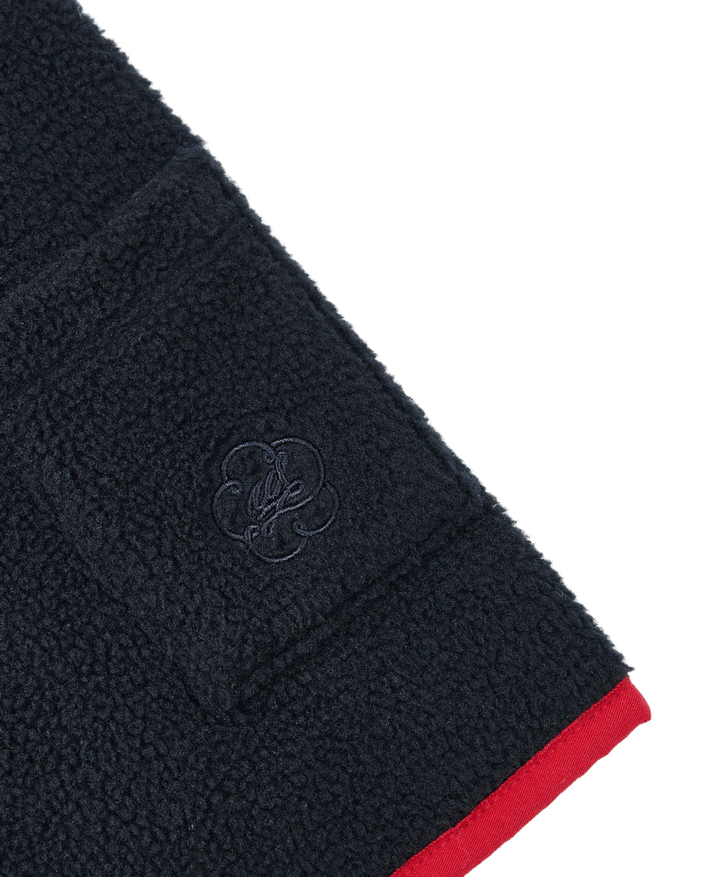 A close-up of the NAVY TEARDROP KNOT FLEECE by Sundae School showcases its cozy fleece fabric and pocket, which is adorned with an embroidered logo. The edge is accented with a red trim, lending a subtle East Asian-inspired detail.