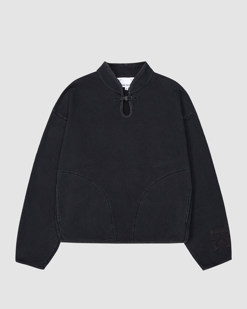 The BLACK TEARDROP KNOT SWEATSHIRT by Sundae School is a black cotton pullover with long sleeves, a short stand collar, V-neckline, drawstring detail, curved front seams, and a sleeve patch. Shown on a plain light gray background.