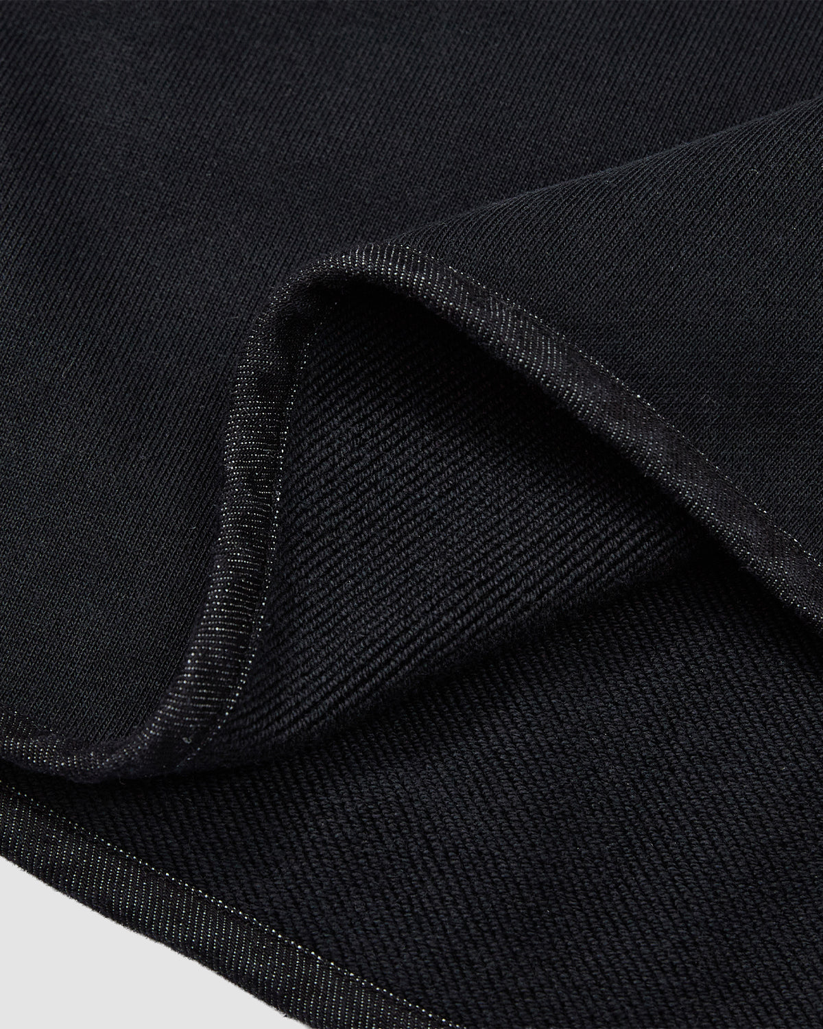 A close-up of the BLACK TEARDROP KNOT SWEATSHIRT by Sundae School shows its black cotton fabric with a distinct twill weave and cleanly finished edges.