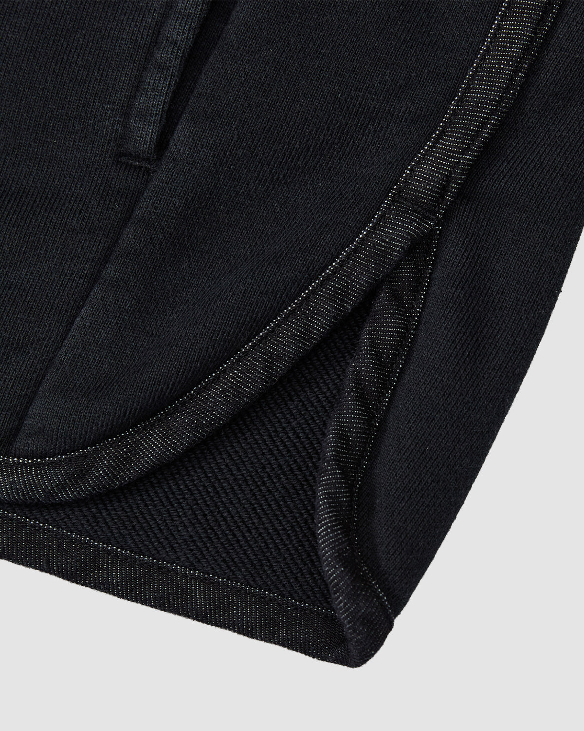 Close-up of the hem and side seam on the BLACK TEARDROP KNOT SWEATSHIRT by Sundae School, showing detailed stitching and texture on black cotton fabric, with one edge slightly overlapping against a light grey background.