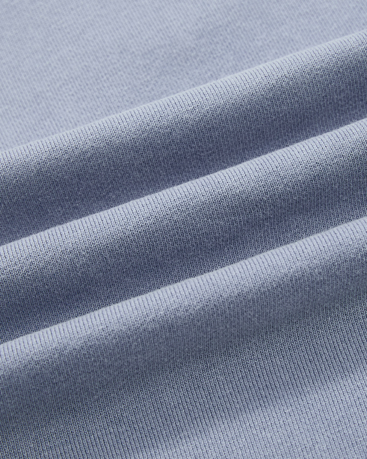 Close-up of the SKY BLUE TEARDROP KNOT SWEATSHIRT by Sundae School: light blue, fine knit fabric with three horizontal folds and a soft 100% cotton texture for comfort.
