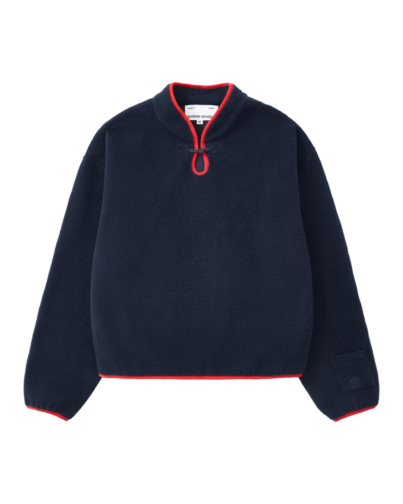 Sundae School’s NAVY TEARDROP KNOT FLEECE is a navy blue cozy fleece pullover featuring long sleeves, red trim on the cuffs, hem, and collar, and a short front zipper with a circular pull tab.