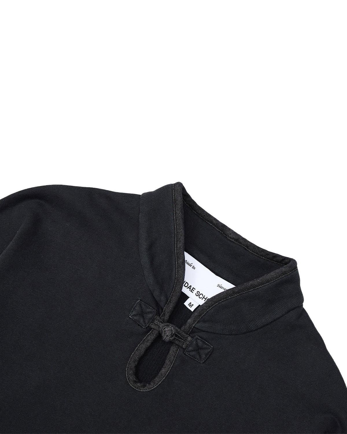 Close-up of the BLACK TEARDROP KNOT SWEATSHIRT by Sundae School, featuring a Mandarin collar and distinctive knotted button closure, highlighting the refined detailing of the design. The inner tag is partially visible with size information and text. The fabric looks soft with a subtle texture.