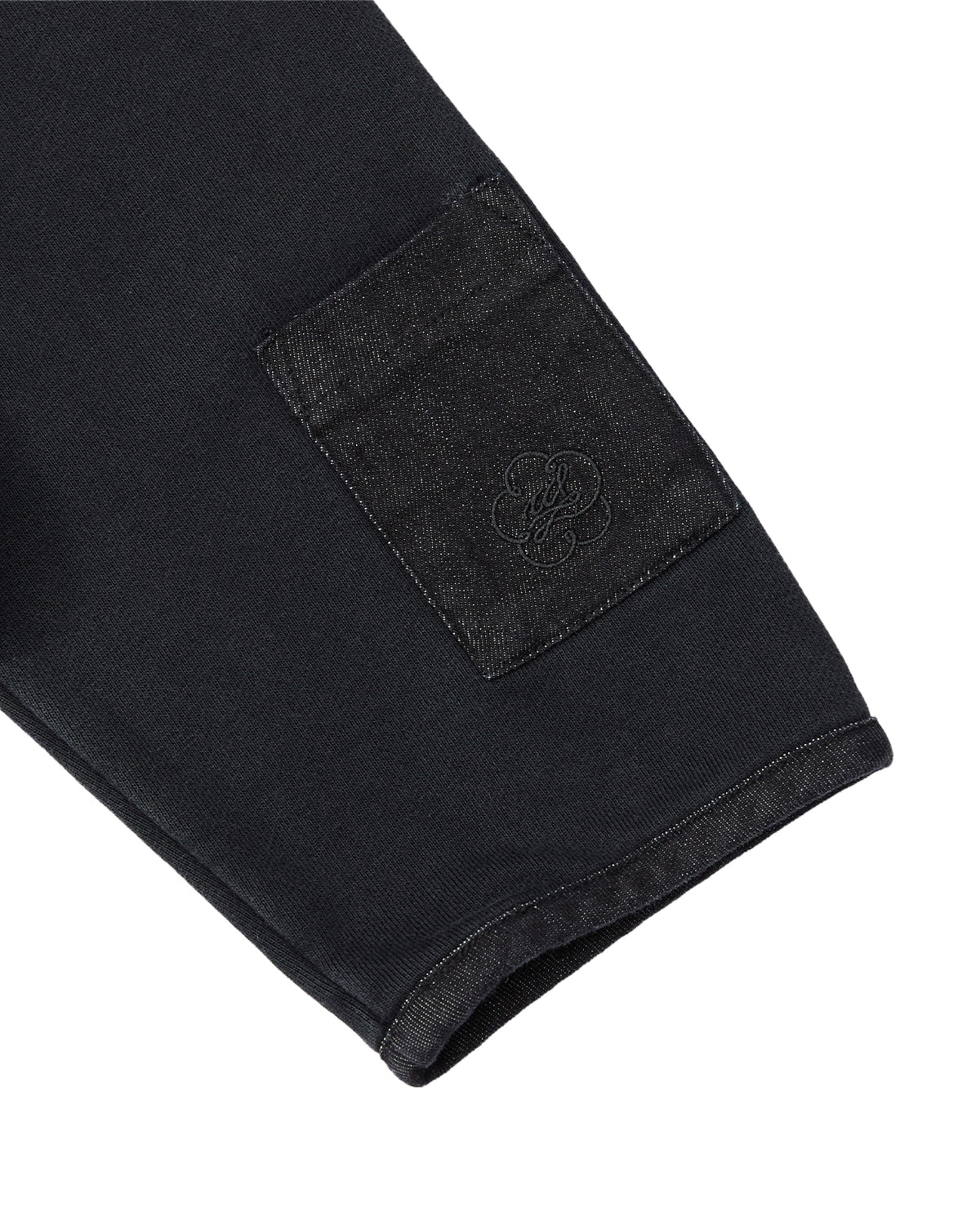 A close-up of the BLACK TEARDROP KNOT SWEATSHIRT by Sundae School shows a sleeve crafted from 100% cotton, featuring a sewn-on rectangular pocket adorned with an embroidered logo on one side. The sweatshirt is finished with visible stitching along the cuff and edges for a refined touch.
