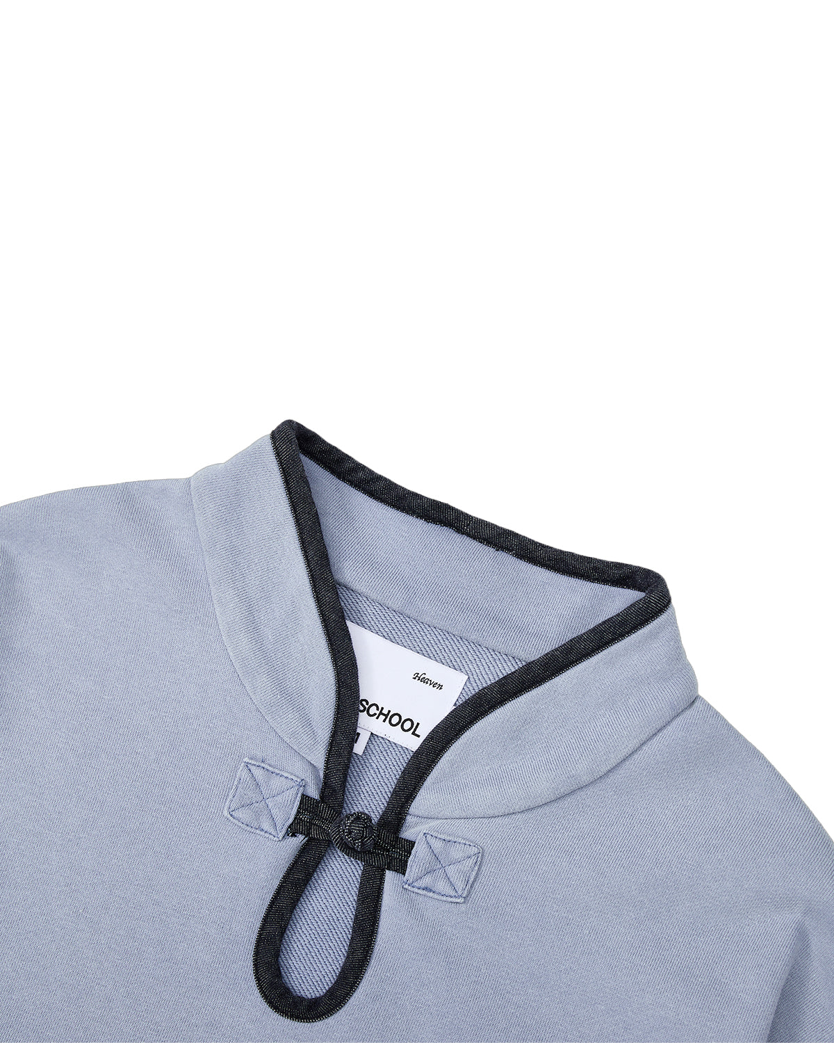 A close-up of the Sundae School SKY BLUE TEARDROP KNOT SWEATSHIRT showcases its light blue 100% cotton fabric, accented by a dark denim trim mandarin collar and a distinctive decorative knotted button at the neckline. A partially visible white inner tag completes the look.