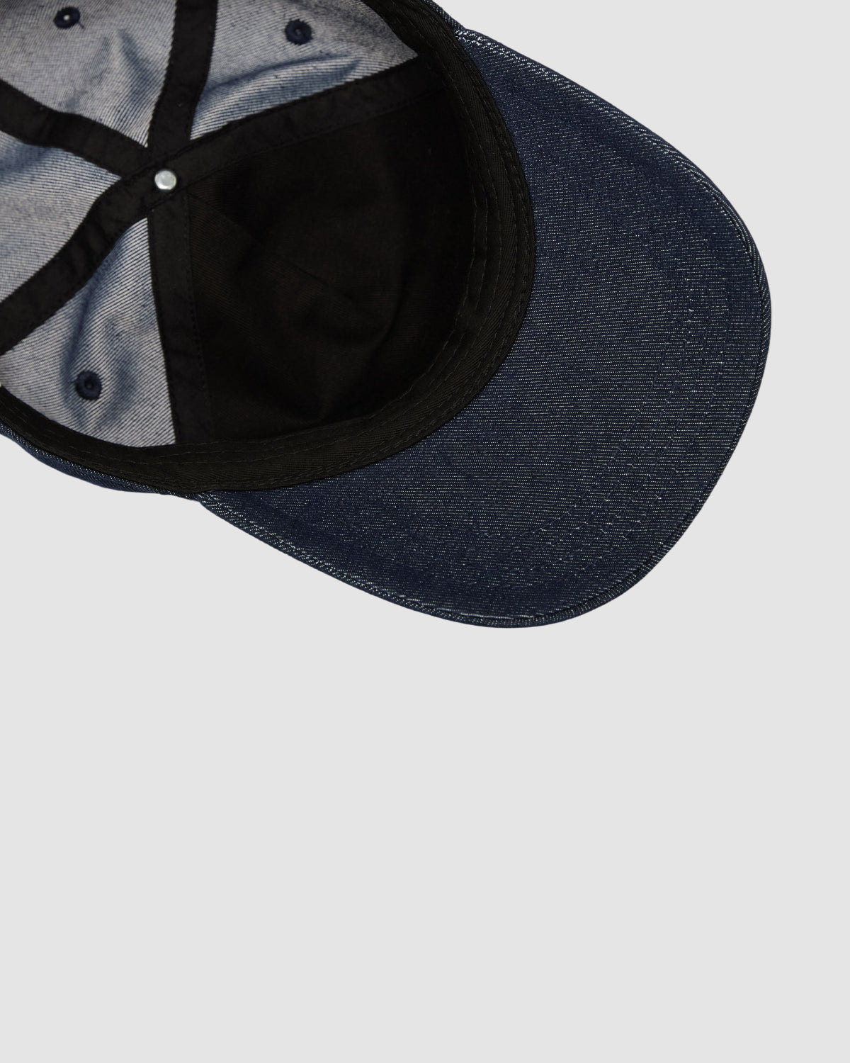Top view of the Sundae School INDIGO DENIM TIGER CAP, a blue denim six-panel strapback hat with a black sweatband, visible stitching, inside lining, and metal crown button on a plain light gray background.