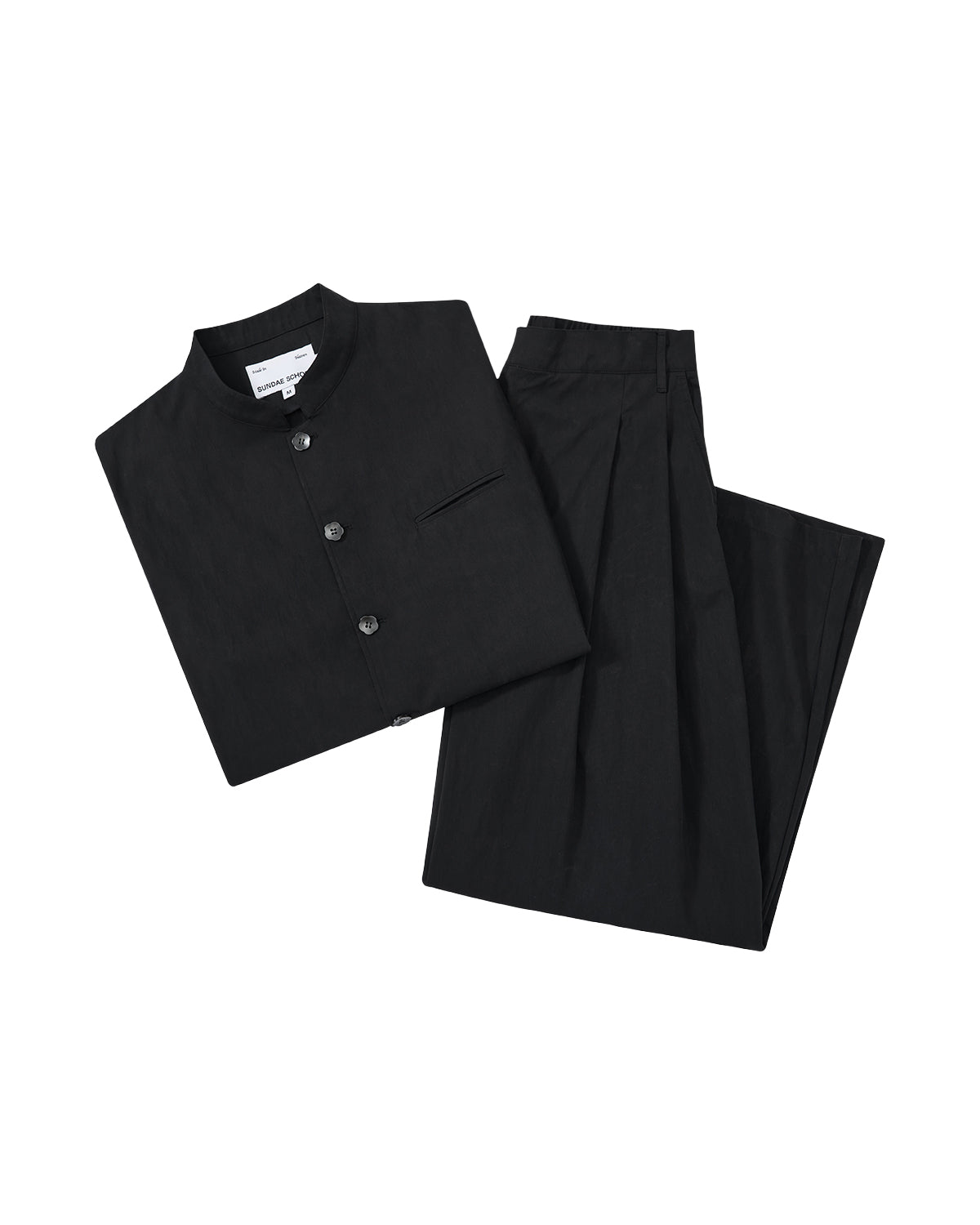 The BLACK PLEATED UNIFORM SLACKS by Sundae School are shown neatly folded with a black mandarin-collar shirt, both displayed on a plain light gray background.