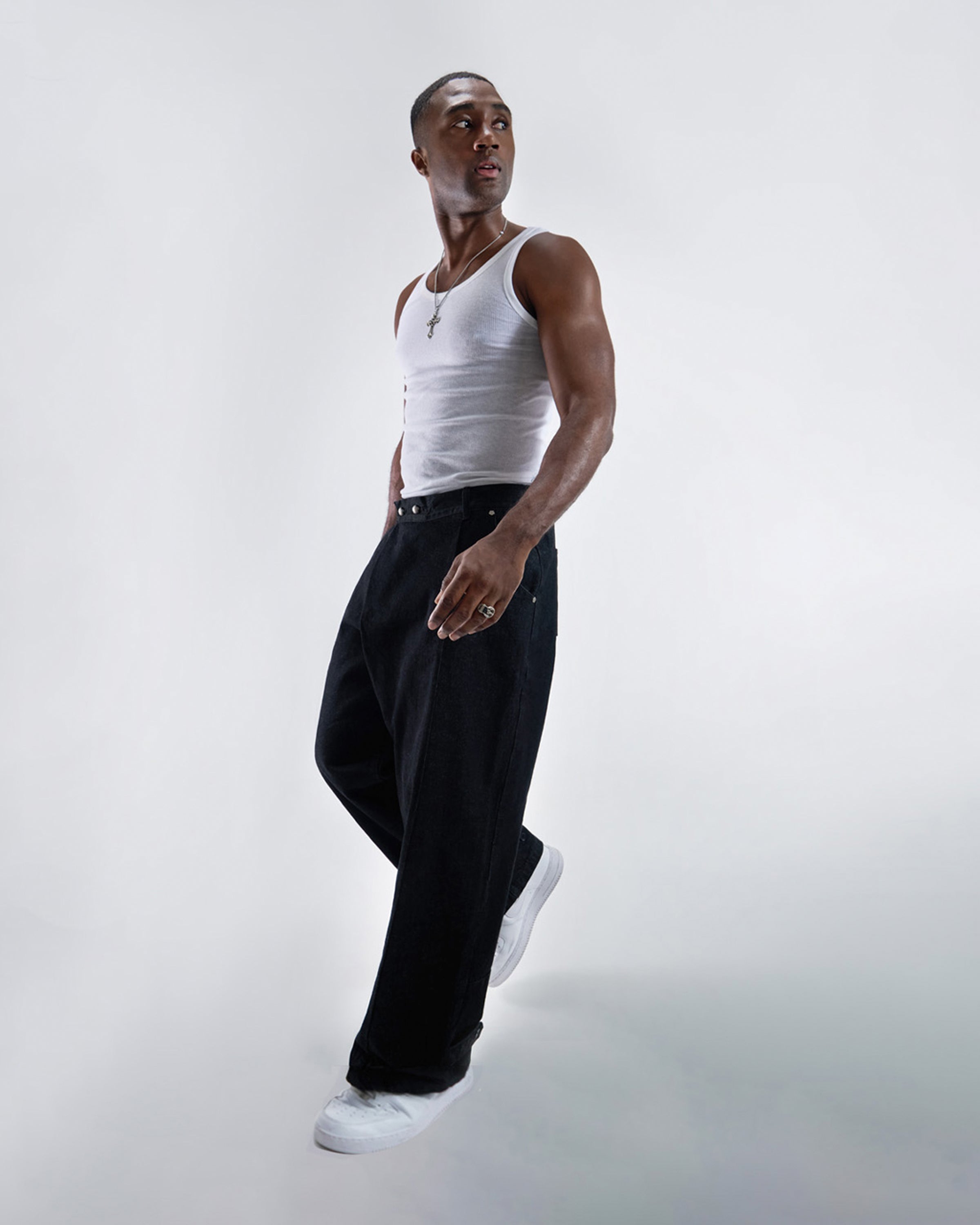 Black wide-leg hanbok denim pants modeled with white ribbed tank top, silver cross necklace and ring accessories, dynamic walking pose with white sneakers against white studio background