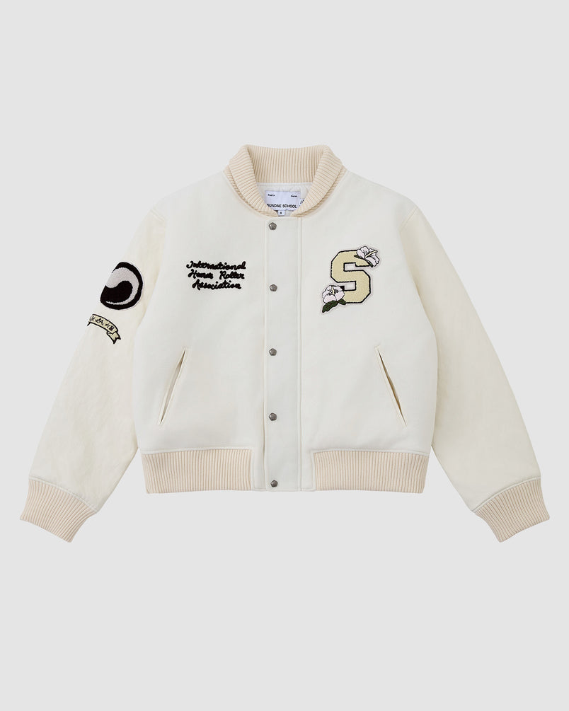 The IVORY VARSITY JACKET by Sundae School features a cream oversized fit, ribbed beige details, vegan leather sleeves, snap buttons, and embroidered patches—including a large S and “International House Dance Association” text—for unisex streetwear style.