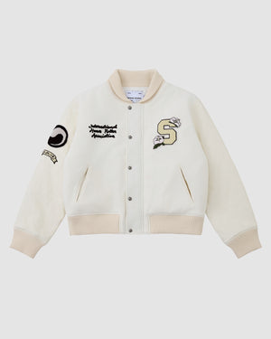 The IVORY VARSITY JACKET by Sundae School features a cream oversized fit, ribbed beige details, vegan leather sleeves, snap buttons, and embroidered patches—including a large S and “International House Dance Association” text—for unisex streetwear style.