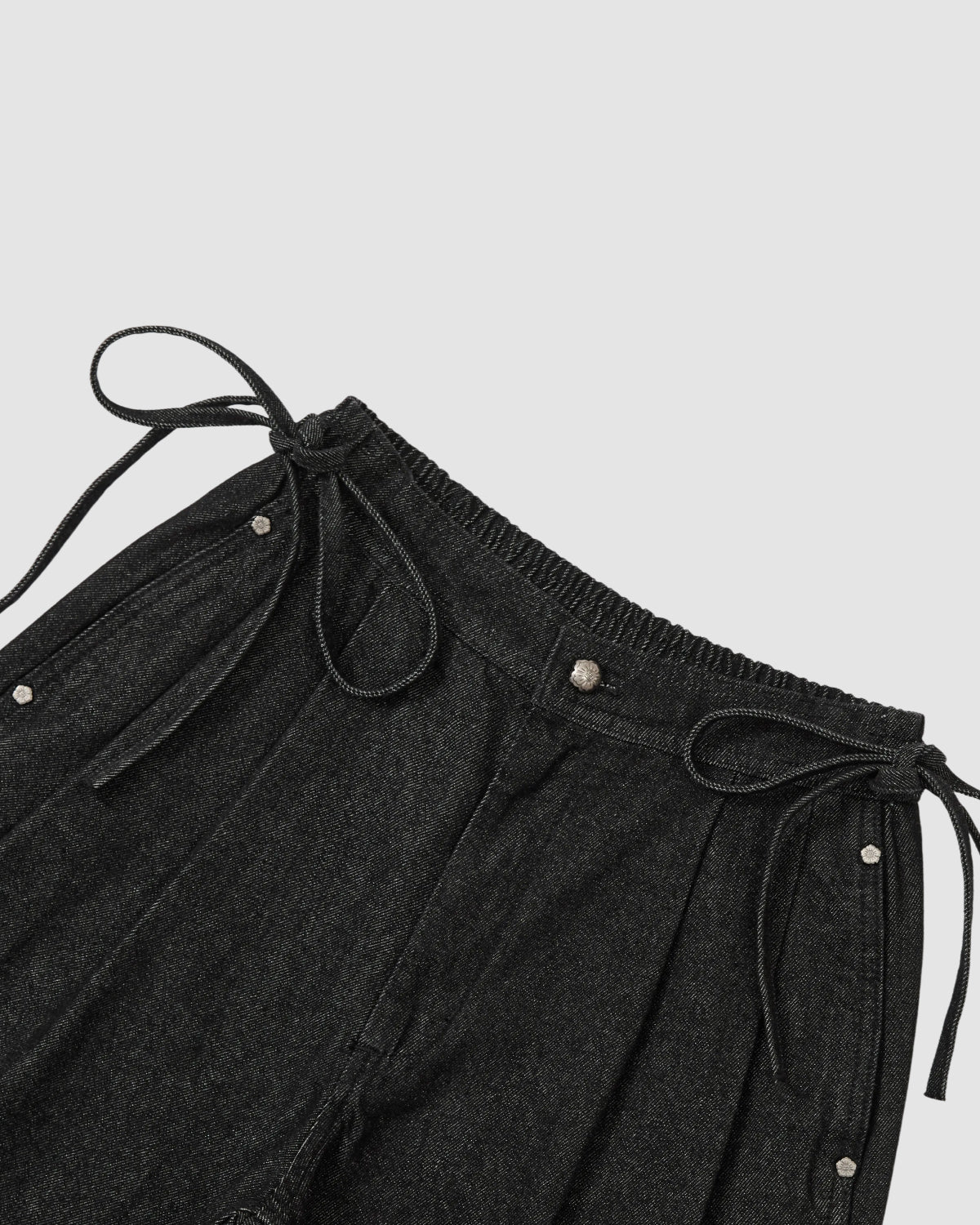 Close-up of BLACK VITA JORTS by Sundae School: black drawstring shorts with an elastic waistband, silver snap buttons, and side pockets—ideal for lovers of elastic waist styles—shown on a light gray background.