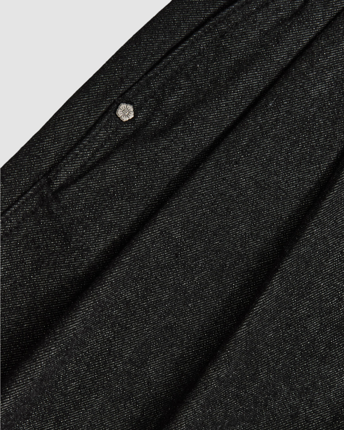 Close-up of the BLACK VITA JORTS by Sundae School, featuring dark gray textured fabric with a metallic button detail, subtle sheen, and visible pocket—showcasing the unique style of these wide-leg denim shorts.
