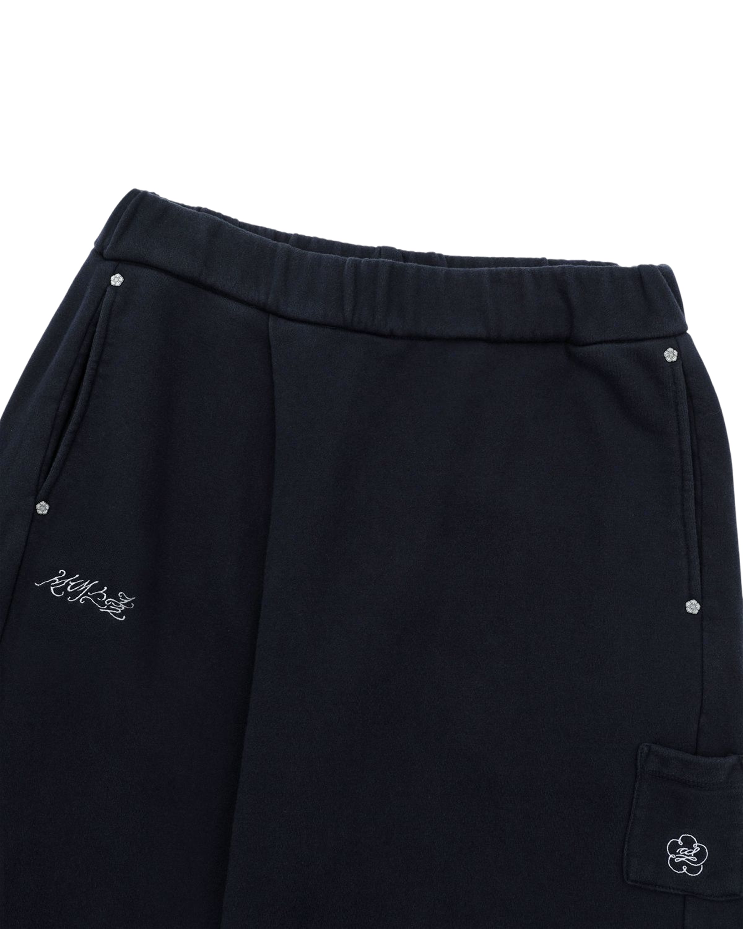 Navy unisex joggers by Sundae School, featuring silver snap buttons, a small embroidered script on one pocket, and a side pocket adorned with a small cartoon character patch. Made from soft cotton sweatpants material, these NAVY WASH WRAP SWEAT BAJI have an elastic waistband for added comfort.
