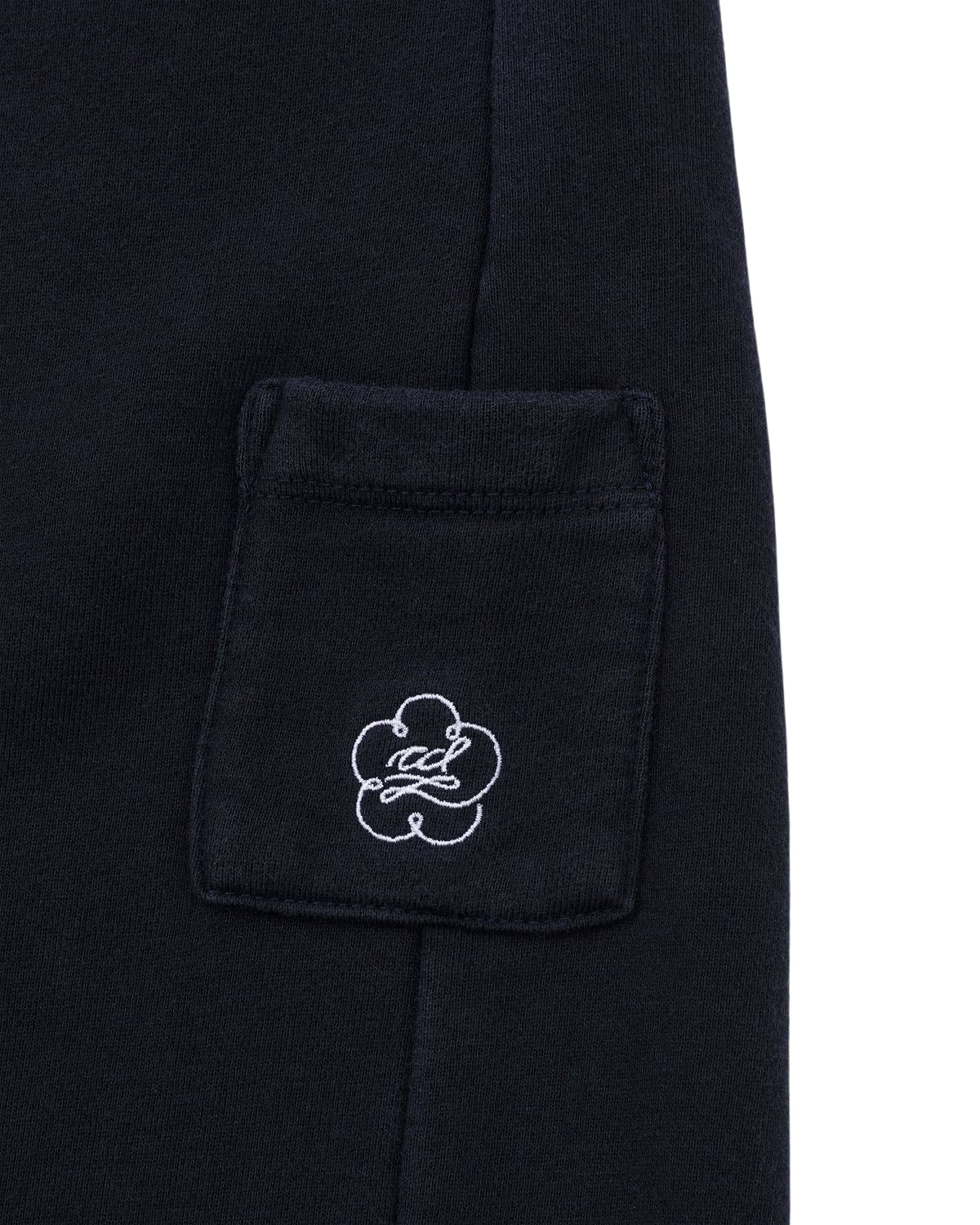 A close-up of a small, square black fabric pocket with white embroidery featuring Sundae School’s flower-like logo and cursive text on dark clothing, seamlessly complementing the relaxed style of the NAVY WASH WRAP SWEAT BAJI wrap-front pants.