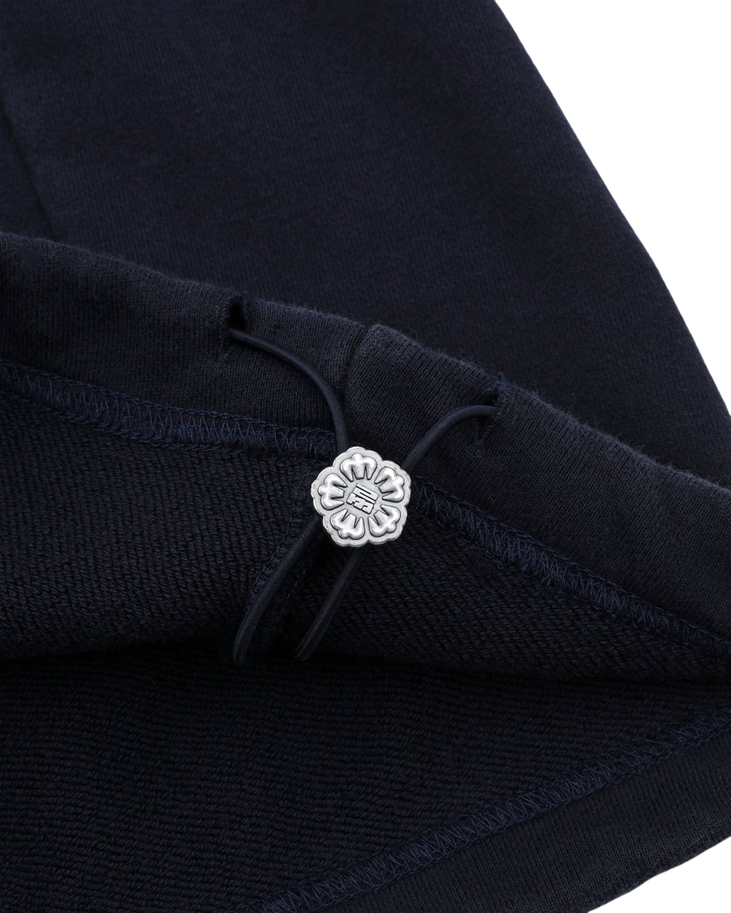 Close-up of the dark navy fabric from Sundae School's NAVY WASH WRAP SWEAT BAJI, featuring a silver flower-shaped button and black drawstring detail, highlighting the stitching and texture.