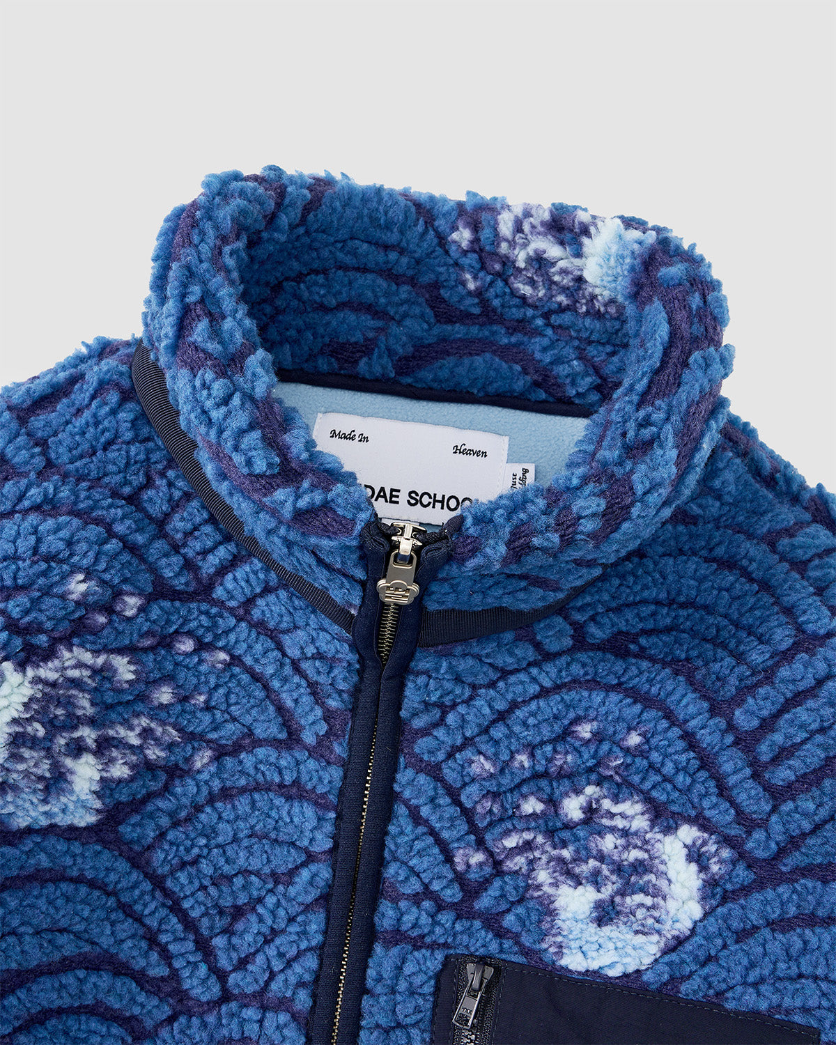 Close-up of Sundae School's BLUE WAVE FLEECE, a blue pile jacket with a custom wave-motif jacquard, textured wave-like pattern, high collar, front zipper, and a small inner collar tag.