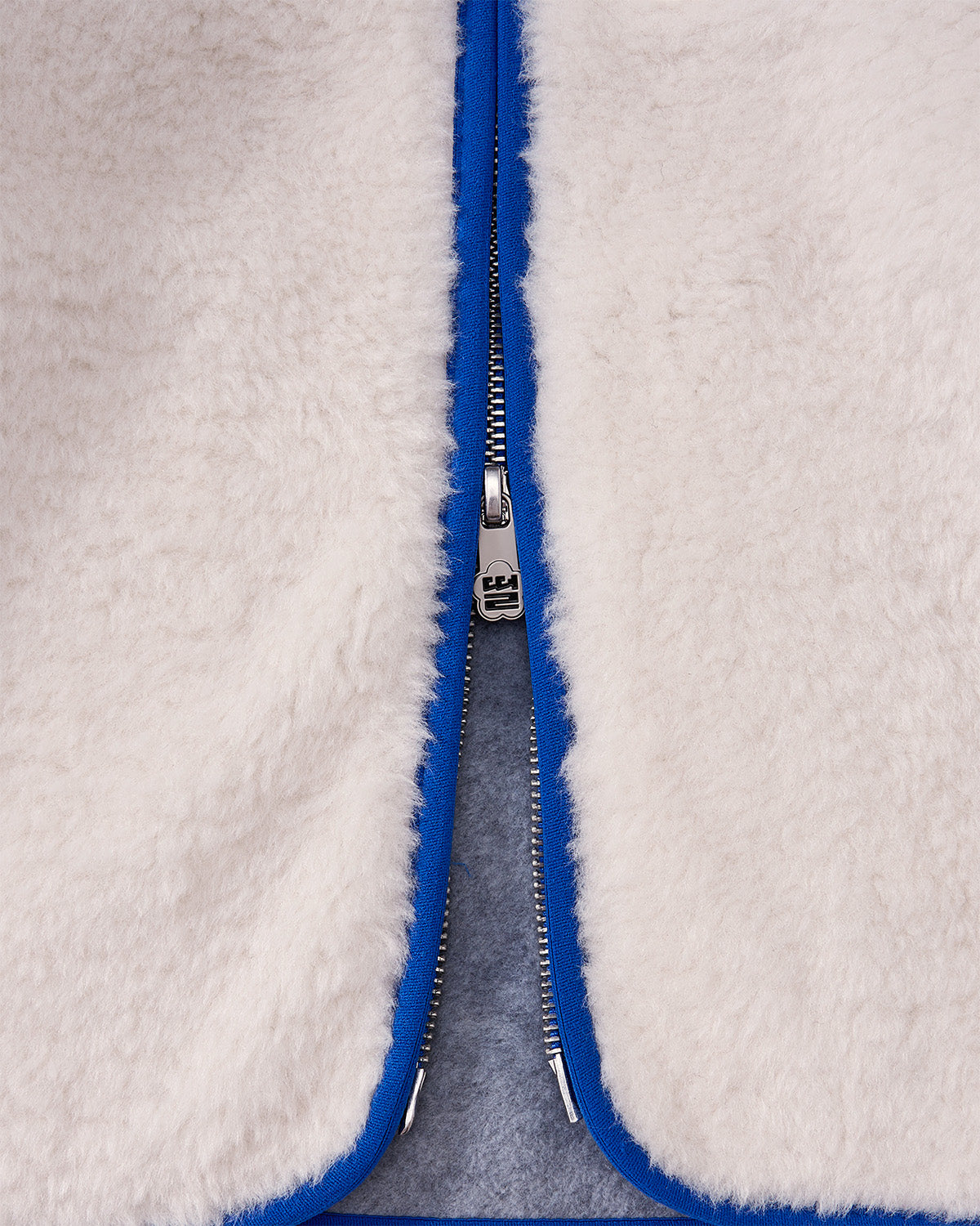 Close-up of the IVORY MUGUNGHWA FLEECE by Sundae School, a white sherpa jacket featuring a partially unzipped silver zipper and bright blue trim along the edges.