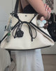A video demonstrating how to pack and style a cream-colored Sundae School canvas tote bag trimmed in black. A person packs everyday essentials like a tablet, planner, journal, Mochi gummies, and sunglasses into the bag's organized compartments, then models different ways to wear and carry the tote.