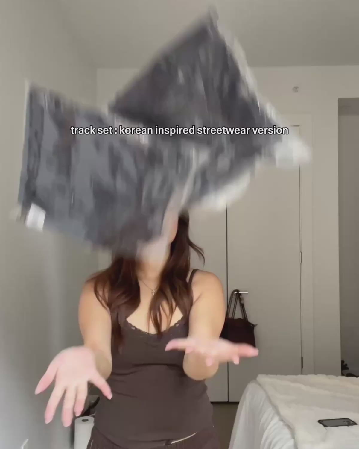 An unboxing and try-on video of a dark navy, Korean-inspired streetwear track set from Sundae School. A woman puts on relaxed wide-leg track pants with zipped ankle details and pairs them with a matching zip-up track jacket. She highlights design features including an embroidered floral emblem on a sleeve stash pocket and a traditional tie-front detail at the high-neck collar.