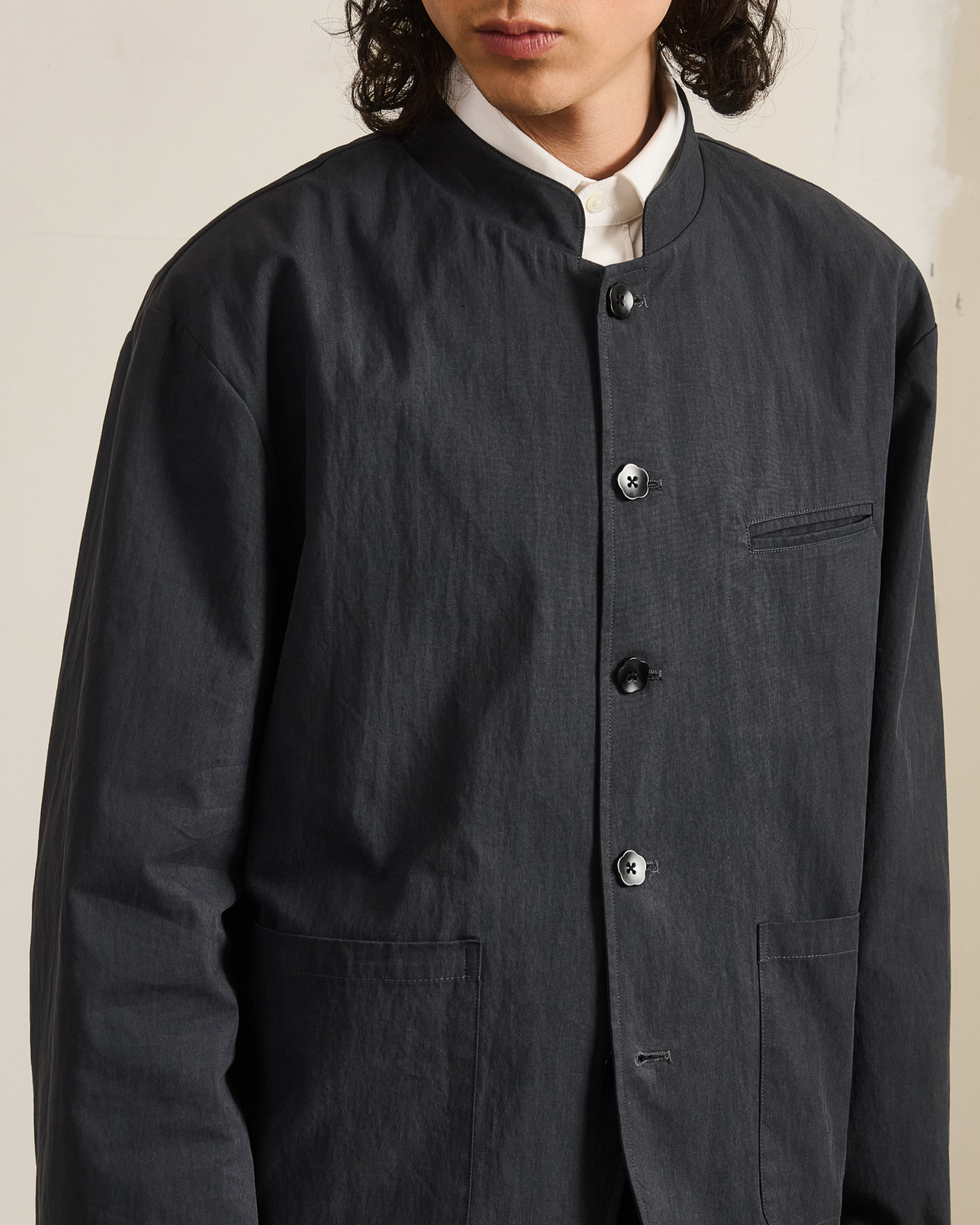 Model wearing charcoal grey stand-collar uniform jacket with welt chest pocket and custom Sundae School flower mochi buttons