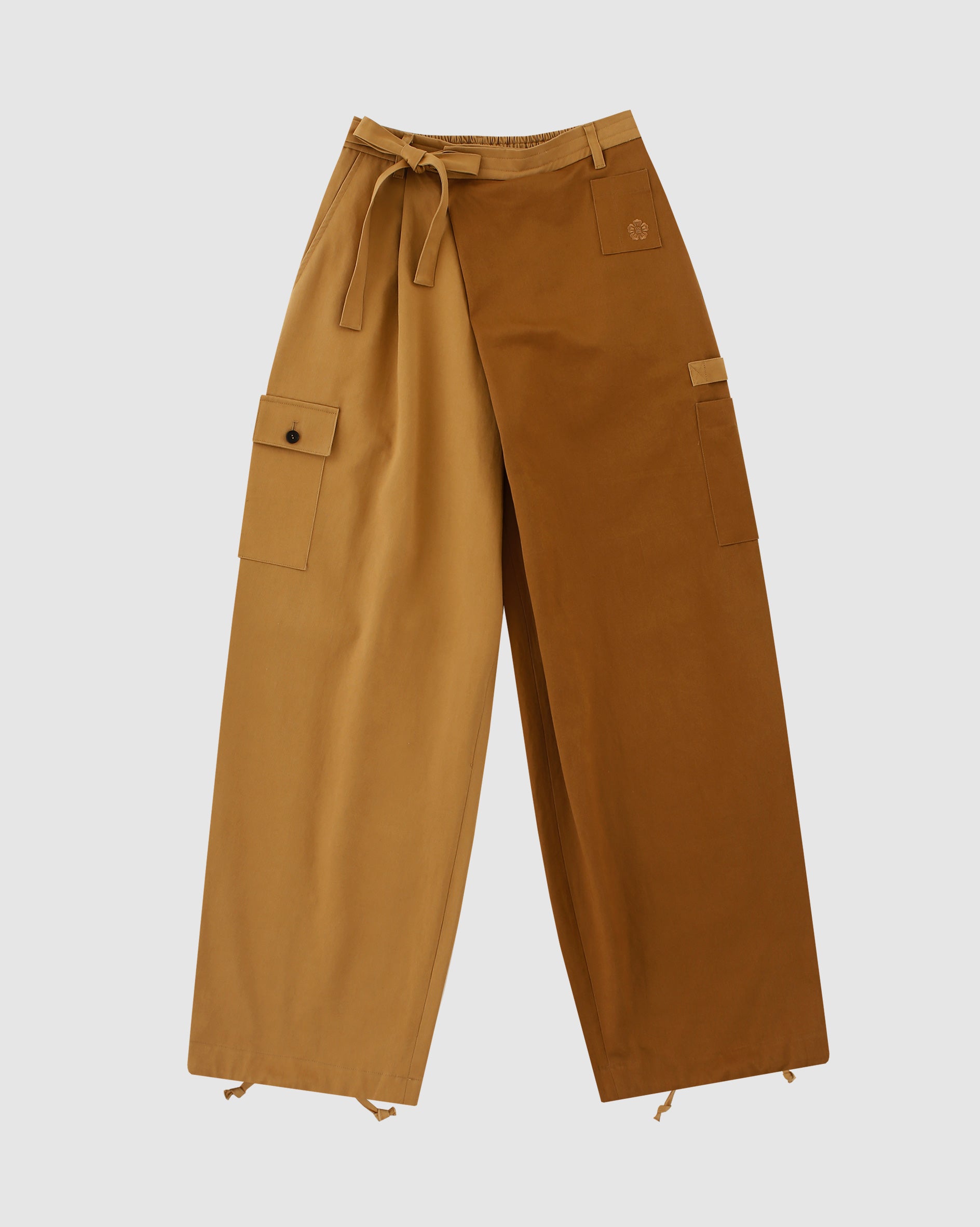 The Tan Pleated Hanbok Cargo Pants by Sundae School feature a wide-leg, two-tone Korean-inspired design with a light brown left side, dark brown right side, pleats, large side pockets, belt loops, and adjustable hems.